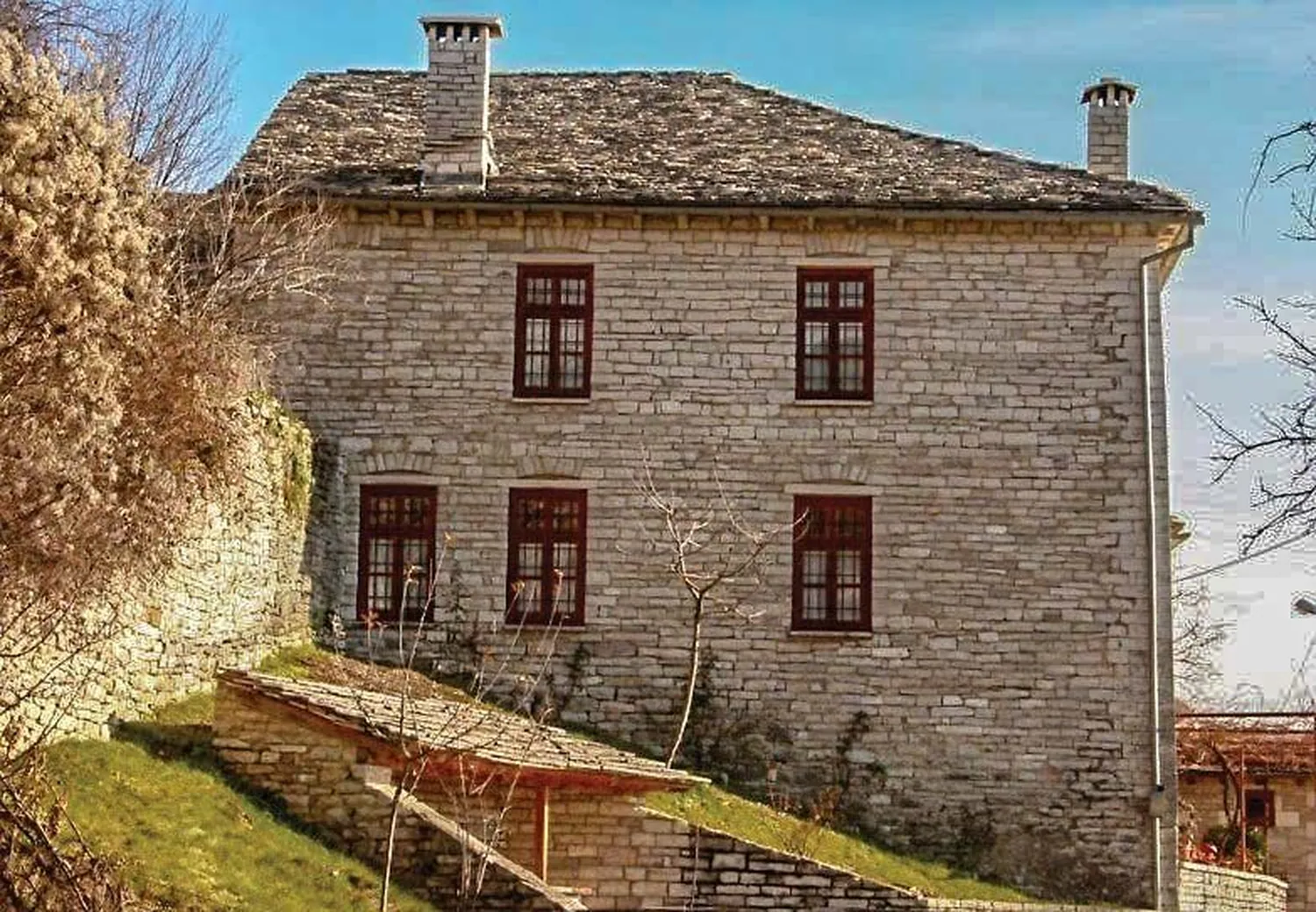 Πέτρινο διώροφο αρχοντικό με πέτρινη στέγη και κόκκινα παράθυρα